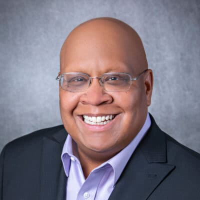 a man wearing a suit and tie smiling at the camera